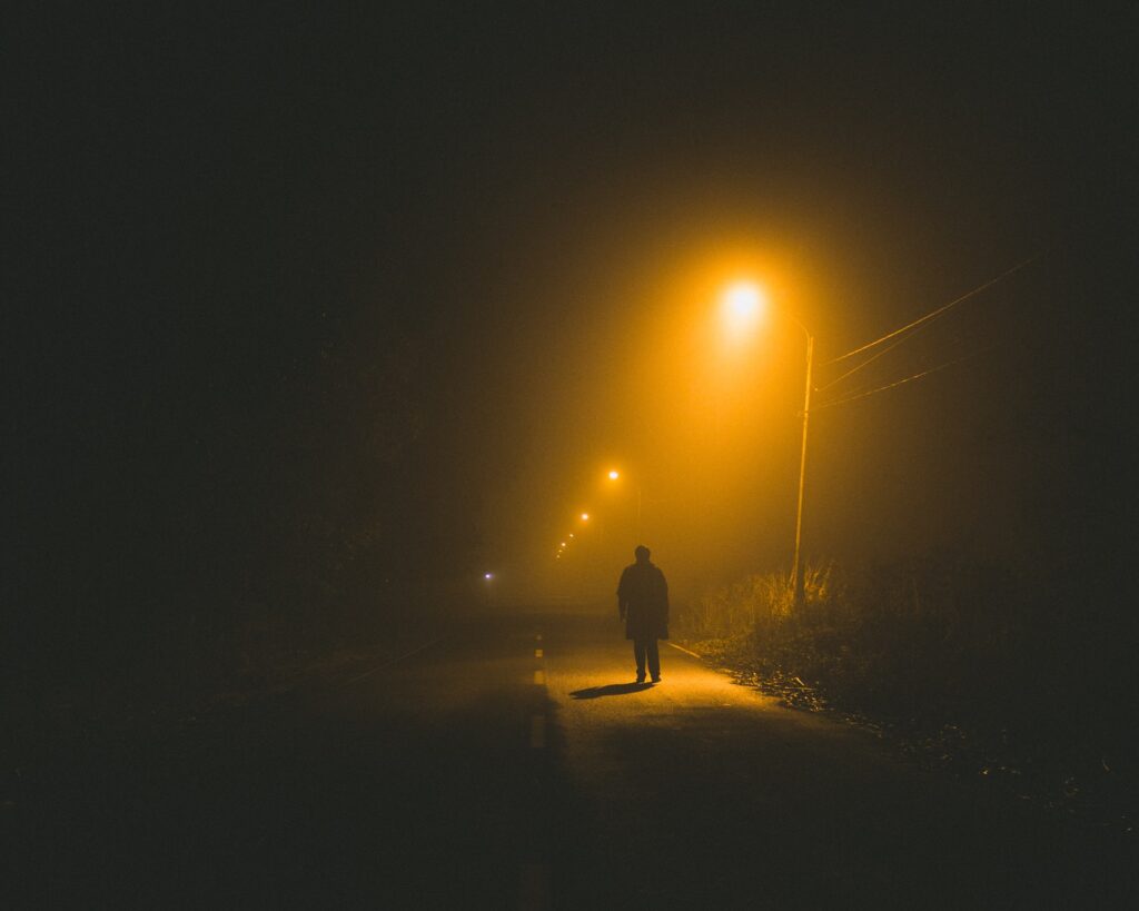 Silhouette of person walking alone under streetlight at night