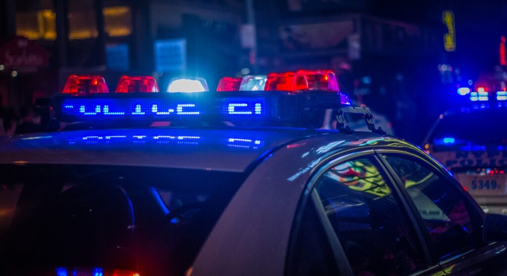 Flashing white, blue, red lights on top of a police car. Blog graphic for blog post for 3 ways to help survive an indoor shooter post for awomansoutlook.com