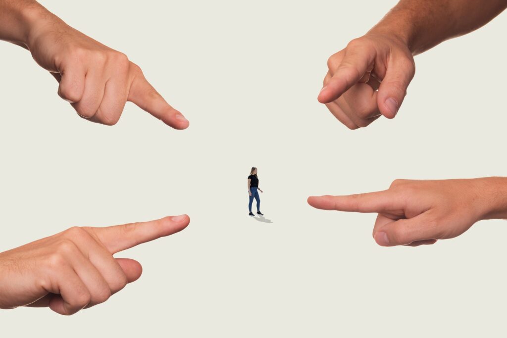 A person is standing in middle of photo with a finger pointing at him from each direction. Blog graphic for blog post from awomansoutlook.com.