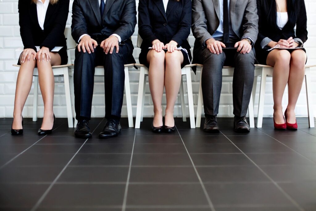 5 sets of legs. 2 men in dress pants. 3 women in skirts. All sitting.  As if wanting for an interview. Blog graphic for blog post How To Find A JOB--Part 2 for awomansoutlook.com
