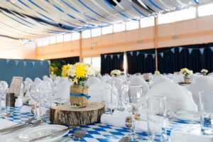 Photo of the inside of a wedding reception held under a tent.  The tables have blue and white checkered table clothes.  Wooden table topper.  Napkins wrapped in wooden napkin holders. Glasses are on the tables too. Blog graphic for blog post 6 Posh Ways To Enjoy A Wedding Reception for awomansoutlook.com