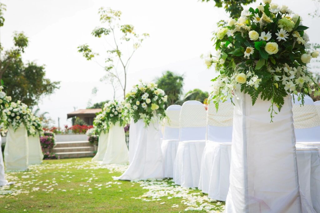 Photo of an outside wedding area with cloth covered chairs, flower sprays, and view of alter.