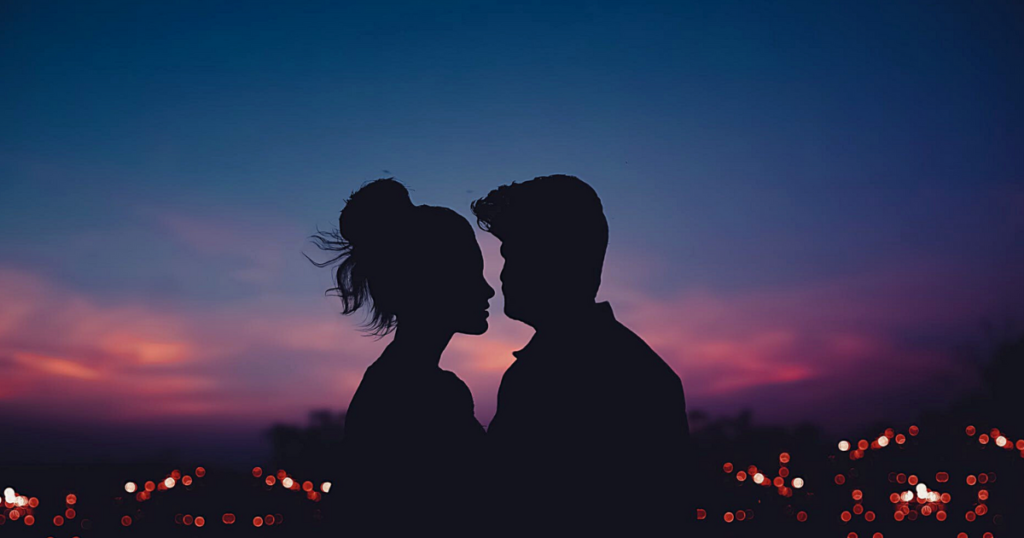 A photo of the profile of a heterosexual couple facing each other against the darking sky above the twinkling lights of a city. Used for the blog post the benefits of abstaining from sex before marriage for blog awomansoutlook.com.