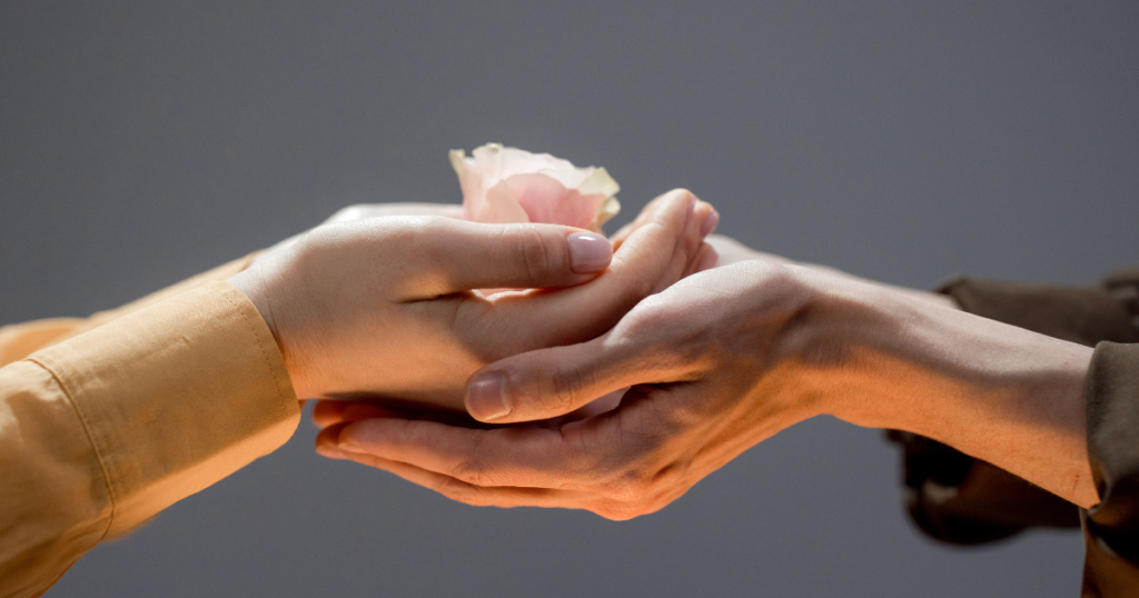Two pairs of hands cupped each other. The top pair holds a rose bud. The blog graphic for blog post how the words be kind can change a life at awomansoutlook.com.